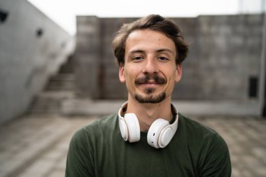 Genç, yetişkin, beyaz erkek, bıyıklı, modern insan portresi. Kulaklık takıyor. Kameraya bakıyor.