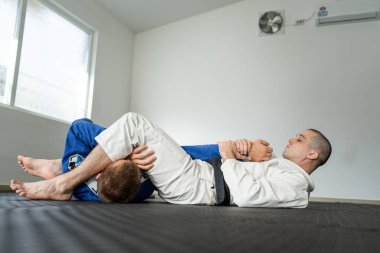 İki sporcu Brezilya jiu jitsu armbar juji gatame sunum kolu BJJ 'i akademide kimono giyim üniformasıyla eğitiyor.