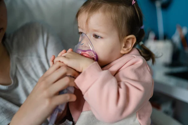 stock image one toddler and mother using nebulizer at home Woman hold her small girl child using vapor steam inhaler mask inhalation at home medical procedure medicament treatment asthma pneumonia bronchitis