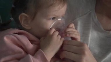 Evde nebulizör kullanan bir çocuk ve anne. Küçük kız çocuğunu buhar spreyi maskesiyle tutuyor. Evde tıbbi müdahale tedavisi görüyor.