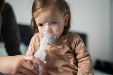 Evde nebulizör kullanan bir çocuk. Buhar buharı soluyan maske kullanan küçük bir kız çocuğu. Evde tıbbi müdahale, astım tedavisi, zatürree bronşit seçici odaklanma.