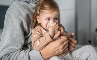 Evde nebulizör kullanan bir çocuk. Buhar buharı soluyan maske kullanan küçük bir kız çocuğu. Evde tıbbi müdahale, astım tedavisi, zatürree bronşit seçici odaklanma.