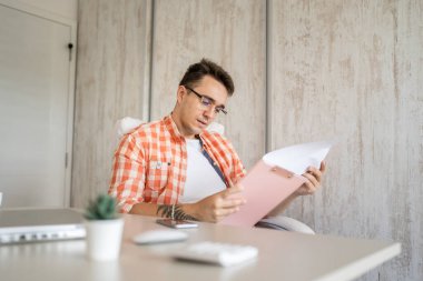 One man male caucasian entrepreneur businessman sitting at office at desk work confident checking paper documents contract or report analyze wear eyeglasses copy space real people