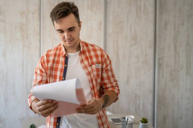 Bir erkek Kafkas girişimci işadamı masabaşında duruyor. Kağıt belgelerini kontrol ediyor ya da gerçek insanları analiz ediyor.
