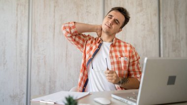 One man freelancer stretch in the office at work sitting in chair at desk using laptop computer having pain sore back suffering from neck ache overwork and exhaustion concept copy space