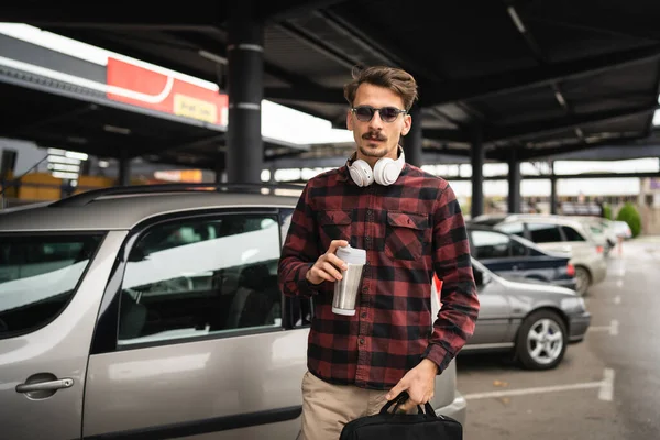 駐車場で車のそばに立っている大人の男性は 仕事中にコーヒーとブリーフケースのカップを待っています — ストック写真