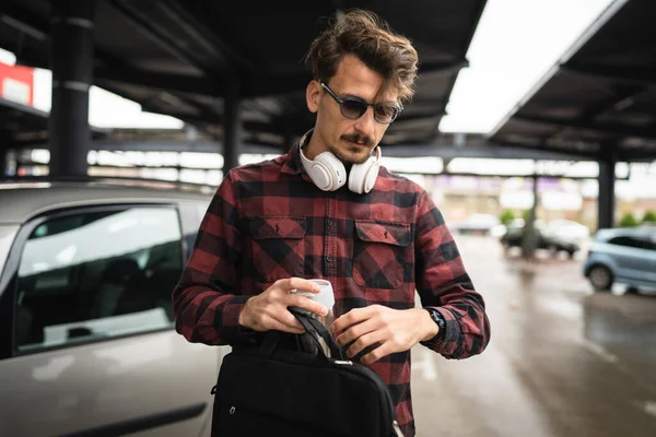 駐車場で車のそばに立っている大人の男性は 仕事中にコーヒーとブリーフケースのカップを待っています — ストック写真