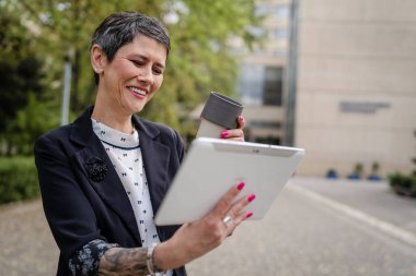 Üst düzey yetişkin bir kadın dijital tablet kullanıyor. Uzaktan kumandalı internet üzerinde çalışıyor. Posta gönderiyor ya da okuyor.