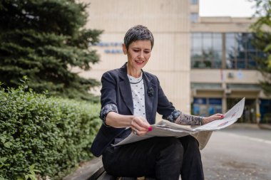 Yetişkin bir kadın yetişkin kadın Kafkas emeklisi gün içinde bankta tek başına oturuyor. Mutlu gazete gülüşü okuyor. Gerçek insanlar uzay emekliliği konseptini kopyalıyor.
