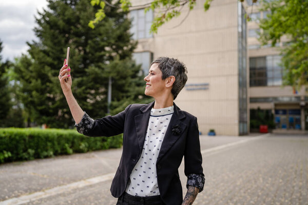 One woman mature or senior caucasian female standing outdoor alone taking selfie photos or making a video call happy smile confident real people modern lifestyle copy space