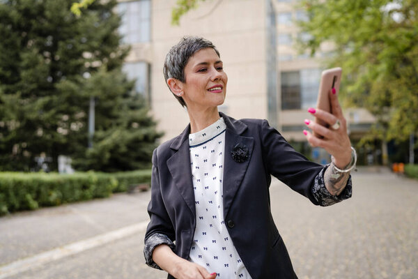 One woman mature or senior caucasian female standing outdoor alone taking selfie photos or making a video call happy smile confident real people modern lifestyle copy space
