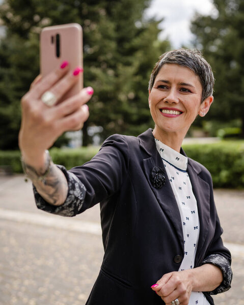 One woman mature or senior caucasian female standing outdoor alone taking selfie photos or making a video call happy smile confident real people modern lifestyle copy space