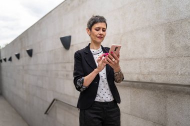Bir kadın modern Kafkasyalı kadın iş kadını cep telefonu kullanıyor. Binanın yanında yürürken telefonla konuşuyor. Beton ya da taş duvara karşı.
