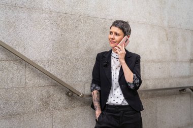 One woman modern mature caucasian female businesswoman using mobile phone making a call talk while walking on the stairs by the building in day against concrete or stone wall real people copy space