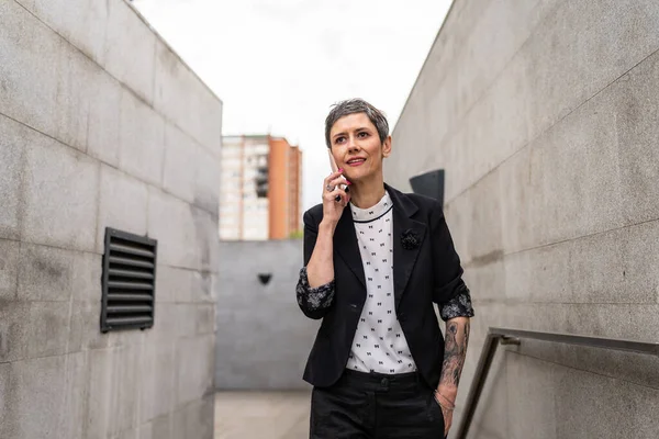 一位现代成熟的女企业家在大楼旁边的楼梯上与混凝土墙或石墙相对照的时候 用手机打了一个电话 — 图库照片