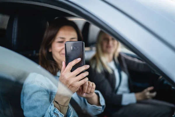 two women drive in a car travel mature caucasian female friends on the road in automobile use mobile phone to take photo real people copy space