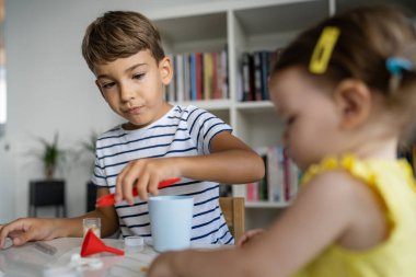 Evde oyuncaklarla oynayan iki çocuk. Bir erkek anaokulu öğrencisi. Küçük kız kardeşiyle birlikte çocukluk deneyleri yapıyor.