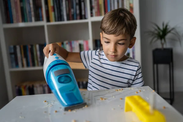 One preschooler boy cleaning mess on the table with hand vacuum cleaner after playing and making experiments helping with home cleaning childhood growing up concept