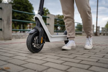 Kimliği belirsiz bir adam ayakta duruyor ya da elektrikli scooter kullanıyor. Gündüz vakti kaldırımda e-scooter kullanıyor. Çevre dostu modern ulaşım.