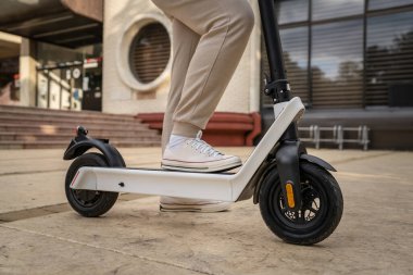 Kimliği belirsiz bir adam ayakta duruyor ya da elektrikli scooter kullanıyor. Gündüz vakti kaldırımda e-scooter kullanıyor. Çevre dostu modern ulaşım.