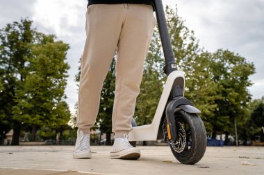 Kimliği belirsiz bir adam ayakta duruyor ya da elektrikli scooter kullanıyor. Gündüz vakti kaldırımda e-scooter kullanıyor. Çevre dostu modern ulaşım.