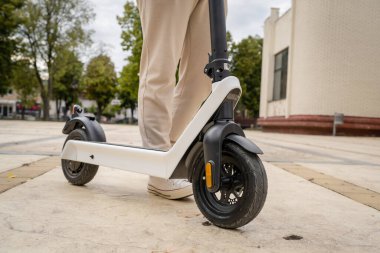Kimliği belirsiz bir adam ayakta duruyor ya da elektrikli scooter kullanıyor. Gündüz vakti kaldırımda e-scooter kullanıyor. Çevre dostu modern ulaşım.