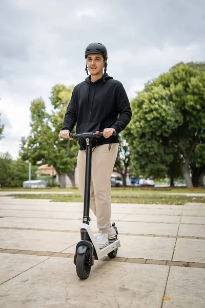 one man young adult caucasian male standing on electric kick scooter in day riding driving in town or city e-scooter eco friendly mode of transport real people copy space full length