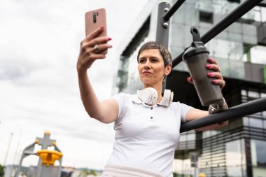 Beyaz bir kadın açık hava antrenmanı sırasında fren yapıyor. Açık hava spor salonunda barlarda dinleniyor. İçme suyu ya da takviye su ile dinleniyor.