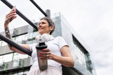 Beyaz bir kadın açık hava antrenmanı sırasında fren yapıyor. Açık hava spor salonunda barlarda dinleniyor. İçme suyu ya da takviye su ile dinleniyor.