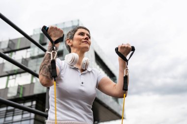 Bir kadın olgun ya da yaşlı, kauçuk elastik direnç bantlı beyaz kadın eğitimi. Açık spor salonunun spor salonundaki tüplerde. Sağlıklı yaşam tarzı konsepti.