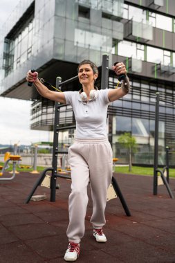 Bir kadın olgun ya da yaşlı, kauçuk elastik direnç bantlı beyaz kadın eğitimi. Açık spor salonunun spor salonundaki tüplerde. Sağlıklı yaşam tarzı konsepti.