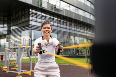 Bir kadın olgun ya da yaşlı, kauçuk elastik direnç bantlı beyaz kadın eğitimi. Açık spor salonunun spor salonundaki tüplerde. Sağlıklı yaşam tarzı konsepti.