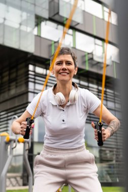 Bir kadın olgun ya da yaşlı, kauçuk elastik direnç bantlı beyaz kadın eğitimi. Açık spor salonunun spor salonundaki tüplerde. Sağlıklı yaşam tarzı konsepti.