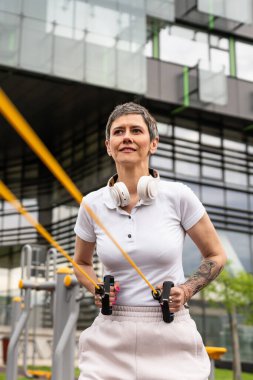 Bir kadın olgun ya da yaşlı, kauçuk elastik direnç bantlı beyaz kadın eğitimi. Açık spor salonunun spor salonundaki tüplerde. Sağlıklı yaşam tarzı konsepti.