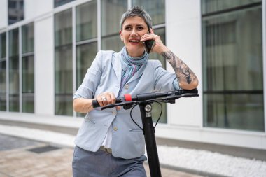 Yetişkin bir yaşlı beyaz kadın dışarıda duruyor. Cep telefonu kullanıyor. Gündüz güvenli modern alternatif ulaşım ve iletişim alanı kopyalama yönteminde elektrikli scooterla konuşuyor.