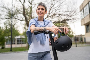 Bir kadın olgun, yaşlı, beyaz, açık havada elektrikli scooterlı bir kadın. Gündüz kendine güvenen bir iş kadını modern alternatif ulaşım yöntemini kullanıyor. Gerçek insanlar uzayı kopyalıyor.