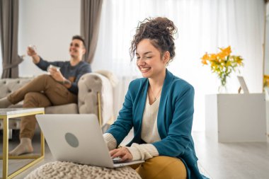 Kadın yetişkin beyaz kadın dizüstü bilgisayarla evde oturuyor kocasıyla arka plan aile kavramı üzerinde çalışıyor mutlu gülüş serbest esmer ev hayatını kopyalıyor.