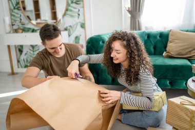 Birkaç erkek ve kadın tatil için hediyeler hazırlıyorlar. Beyaz erkek ve kadın arkadaşlara hediye paketliyor. Paket kağıttan gülücük kutusu kullanıyorlar.