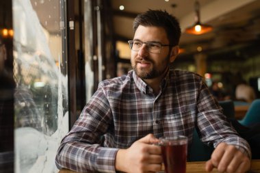 Adult caucasian man sitting alone at cafe front view of one male with beard and eyeglasses holding a cup of tea real people copy space