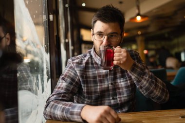 Adult caucasian man sitting alone at cafe front view of one male with beard and eyeglasses holding a cup of tea real people copy space
