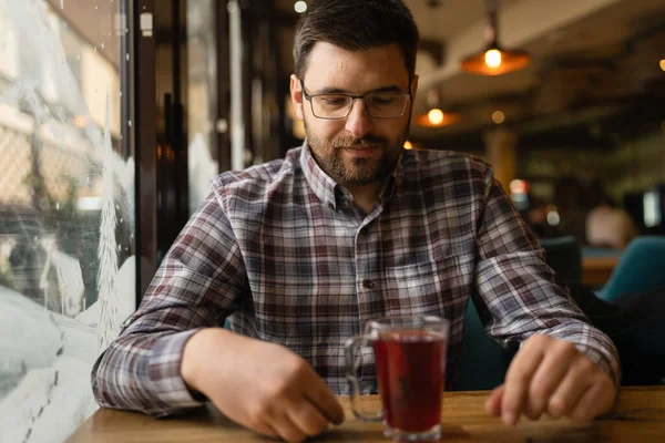 Adult caucasian man sitting alone at cafe front view of one male with beard and eyeglasses holding a cup of tea real people copy space