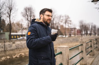 Side view of one adult caucasian man bearded male standing in town in winter cold day holding cup of coffee real people copy space waiting alone real people
