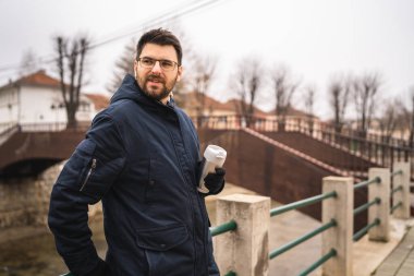 Front view of one adult caucasian man bearded male standing in town in winter cold day holding cup of coffee real people copy space waiting alone real people
