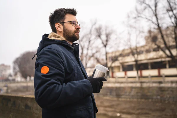 side view of one adult caucasian man bearded male standing in town in winter cold day holding cup of coffee real people copy space waiting alone real people