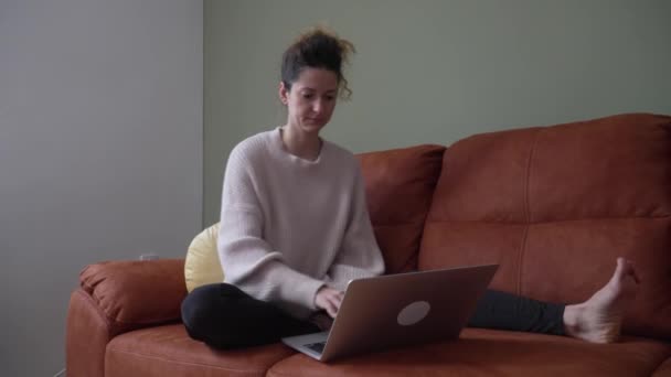 一位成熟的高加索女人坐在家里的沙发床上 在笔记本电脑上工作 或者上网购物 真实的人都会抄袭空间 — 图库视频影像