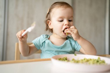 Bir küçük beyaz çocuk evde masada tek başına oturmuş plastik çatal kullanarak yemek yiyor. Çocukluk çağında ve gelişim konseptinde fotokopi uzayı sağlıklı yiyor.