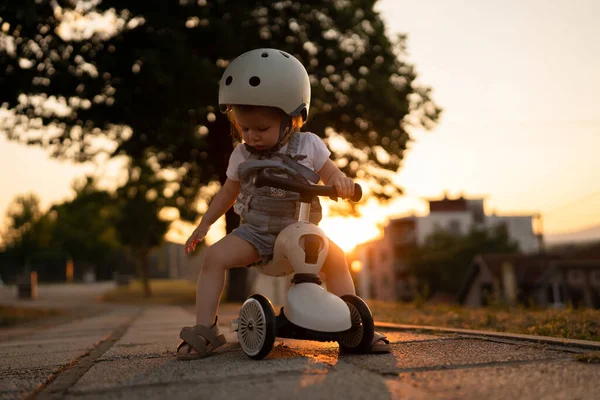 Small caucasian girl toddler playing outdoor in summer evening in sunset with 3 wheel children's kick scooter kid wear protective helmet real people copy space leisure family growing up concept