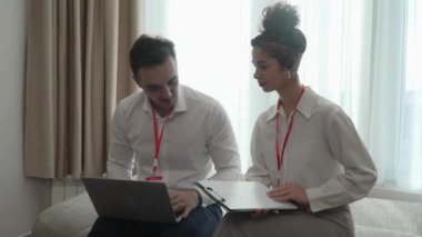 two people man and woman colleagues sitting together at hotel room with contracts and documents preparing for sales meeting or conference making plans sharing experience real people business concept