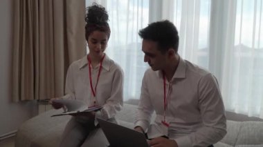 two people man and woman colleagues sitting together at hotel room with contracts and documents preparing for sales meeting or conference making plans sharing experience real people business concept