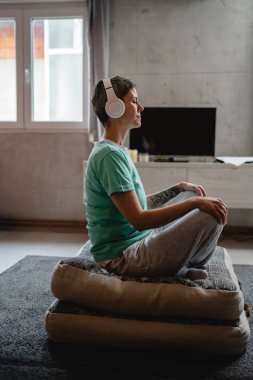 one woman senior caucasian female using headphones for online guided meditation practicing mindfulness yoga with eyes closed on the floor at home real people self care concept copy space